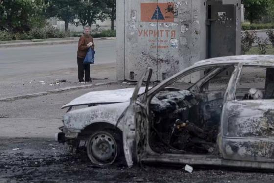 Mulher ao lado de um carro queimado com o corpo de uma pessoa, após um ataque de drones russos em Donetsk